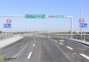 Ulica trzypasmowa i znaki informacyjne oraz ostrzegawcze. W dolnym lewym rogu informacja, że fotografia należy do zbioru Urzędu Gminy Lesznowola