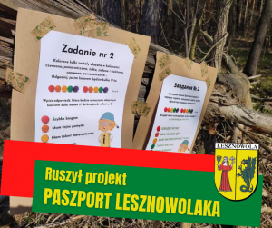 Żółty napis "Ruszył projekt - PASZPORT LESZNOWOLAKA". Herb GMiny Lesznowola w prawym dolnym rogu. Tablice z "Zadaniem nr 2" po polsku i po ukraińsku.