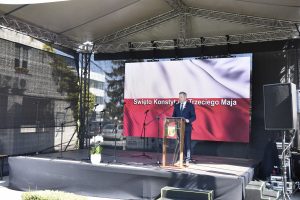 Na scenie Sekretarz Gminy Lesznowola Jan Wysokiński, który prowadził uroczystosć. Tło flaga Polski z napisem Święto Konstytucji 2 Maja