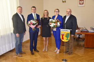 Pięć osób pozuje do zdjęcia. Dwie osoby trzymają kwiaty.