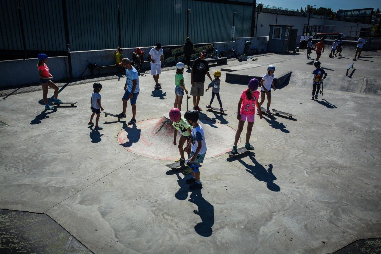 Dzieci jeżdzą na deskach i rolkach na skateparku.