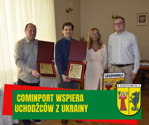 Na zdjęciu stoją 4 osoby, pierwsza i druga od lewej trzymają w rękach otwarte oudełko z tabliczką w środku, na której widać różę. Na dole na zielonym pasku napis: COMINPORT WSPIERA UCHODZCÓW Z UKRAINY. Po prawej na dole herb gminy.