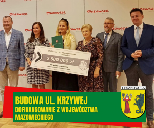 Kilka osób stoi, dwie trzymają podłuzna tablicę informacyjna. Na dole na zielonym pasku napis: BUDOWA UL. KRZYWEJ DOFINANSOWANIE Z WOJEWÓDZTWA MAZOWIECKIEGO.