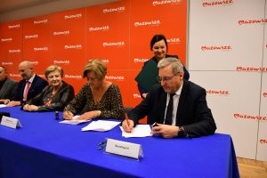 Osoby siedzą za stołem przykrytym fioletowa tkanina. Podpisywanie dokumentów