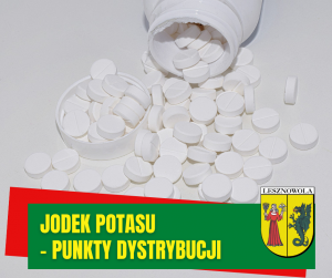 na szarym polu białe tabletki wysypujące się z białego pojemnika, na zielonym polu napis: JODEK POTASU - PUNKTY DYSTRYBUCJI. Obok herb gminy.