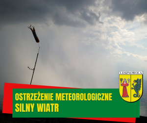 Szare niebo, sygnalizator wiatru. Na dole na zielonym pasu napis: Ostrzeżenie meteorologiczne silny wiatr. Po prawej na dole herb gminy.