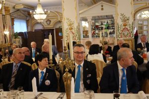 Osoby w garniturach siedzą za stołami.