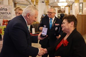 Mężczyzna ściska rękę kobiecie. W tle znajduję się jeszcze jedna kobieta i mężczyzna.