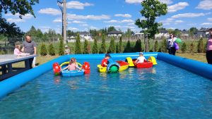 Troje dzieci siedzi w dmuchanych pojazdach i pływa w basenie.