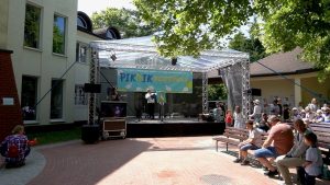 Scena stoi przed kościołem. Ludzie siedzą na ławkach.