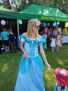 Kobieta w przebraniu księżniczki daje lizaka synkowi. W tle namioty sołectwa.