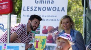 Dziecko, kobieta i mężczyzna uśmiechają się do zdjęcia. W tle baner Gminy Lesznowola.