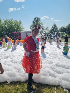 Kobieta w stroju Myszki Mini stoi przed pianą, która wylewa się na ziemie.