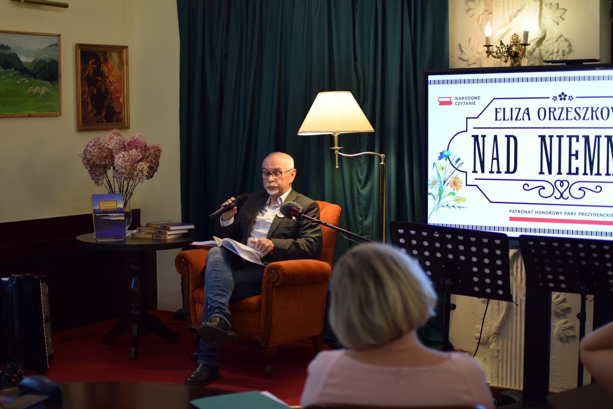 Mężczyzna siedzi na fotelu i czyta "Nad Niemnem".