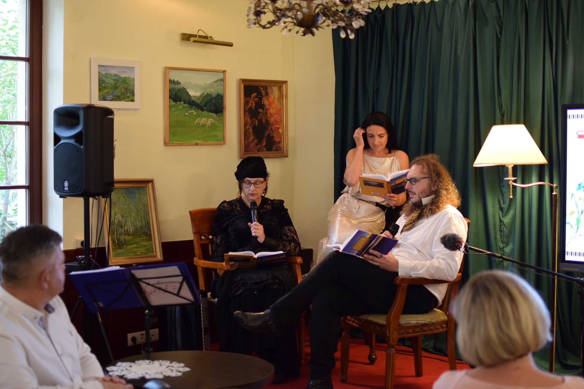 Dwie kobiety i mężczyzna siedzą na fotelach i czytają "Nad Niemnem".