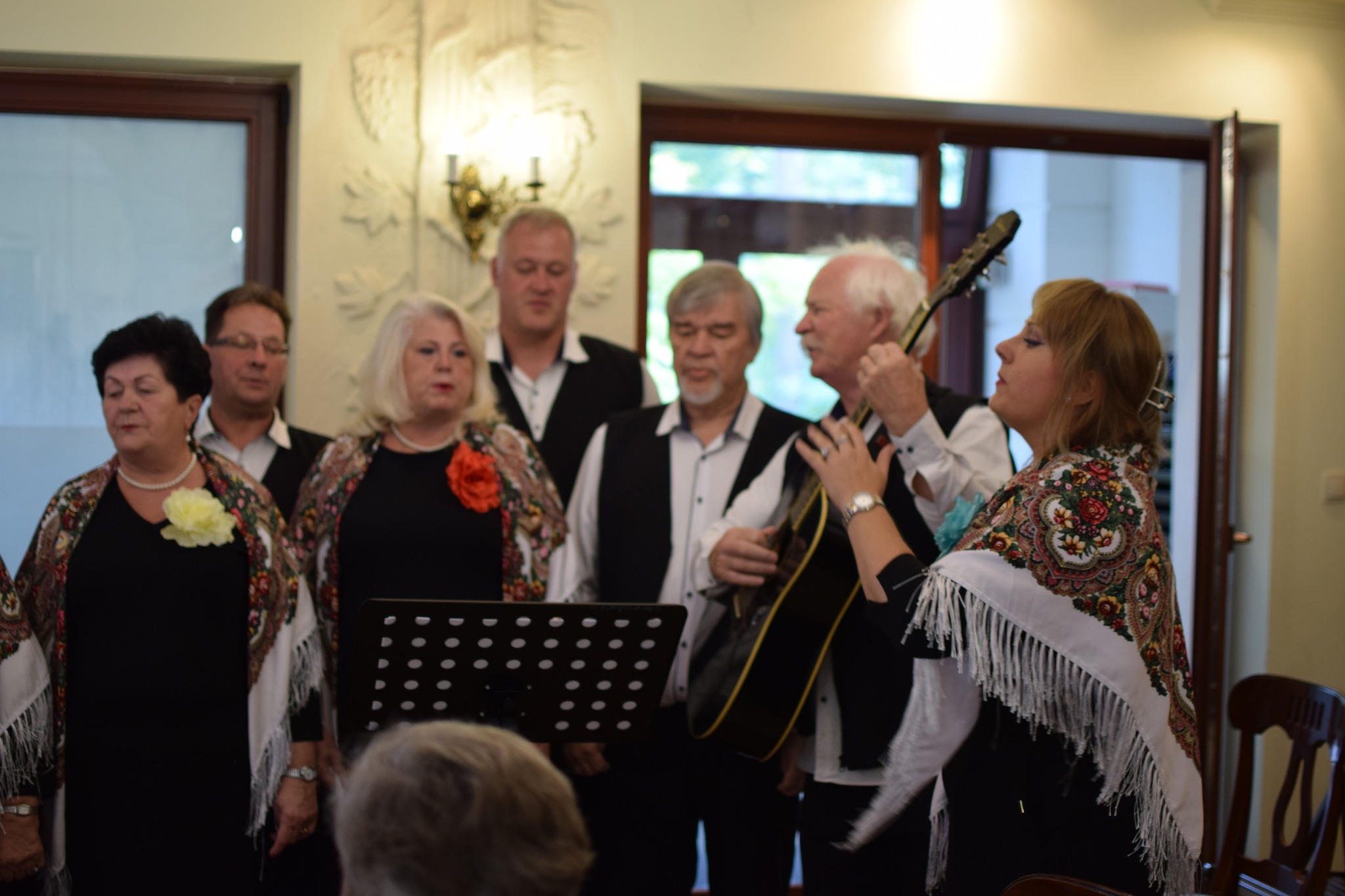 Grupa kobiet i mężczyzn gra i śpiewa w małej sali.