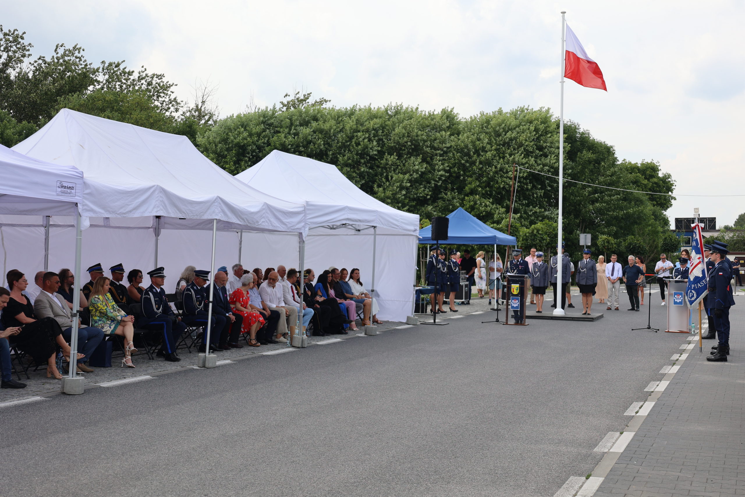 Zgromadzeni goście siedzą na krzesłach pod namiotami