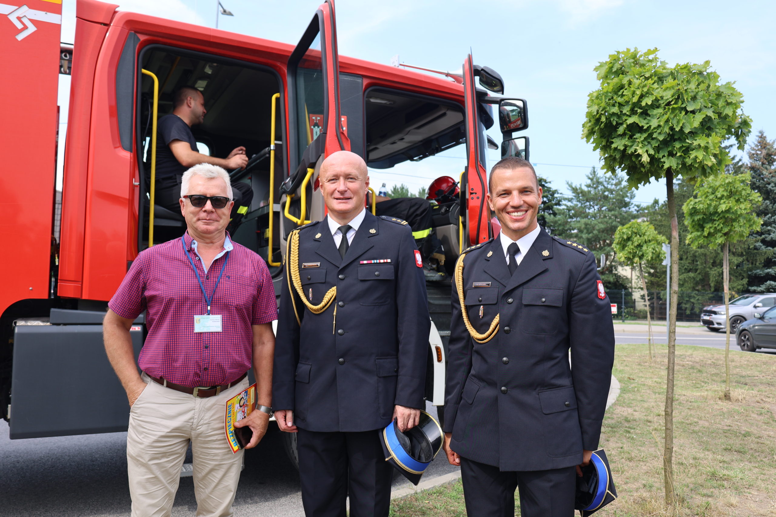 Trzech mężczyzn stoi przed wozem strażackim.