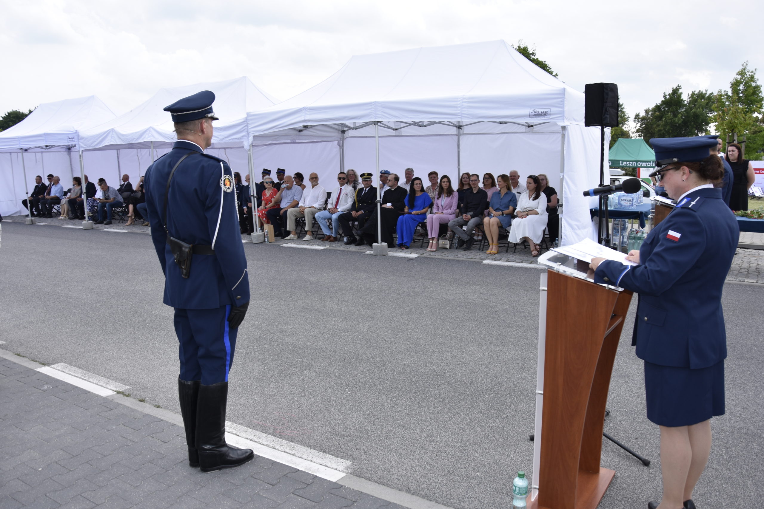 Policjanta przemawia na mównicy. W tle zgromadzeni goście