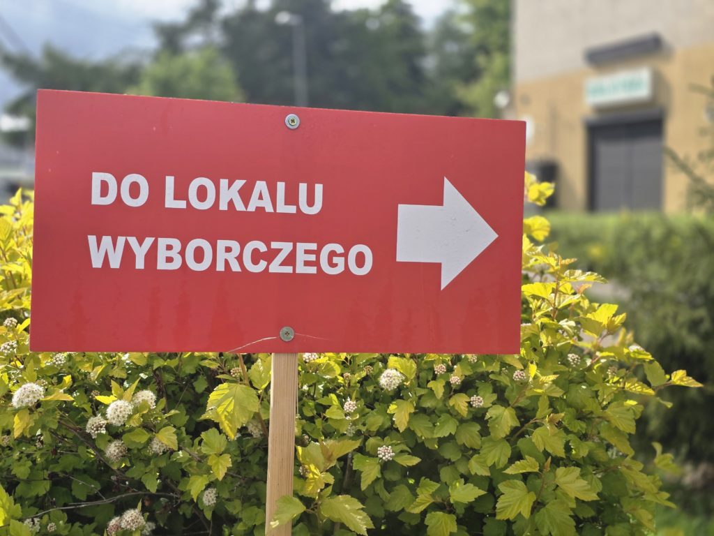 Na zdjęciu czerwona tabliczka z białą strzałką i napisem DO LOKALU WYBORCZEGO