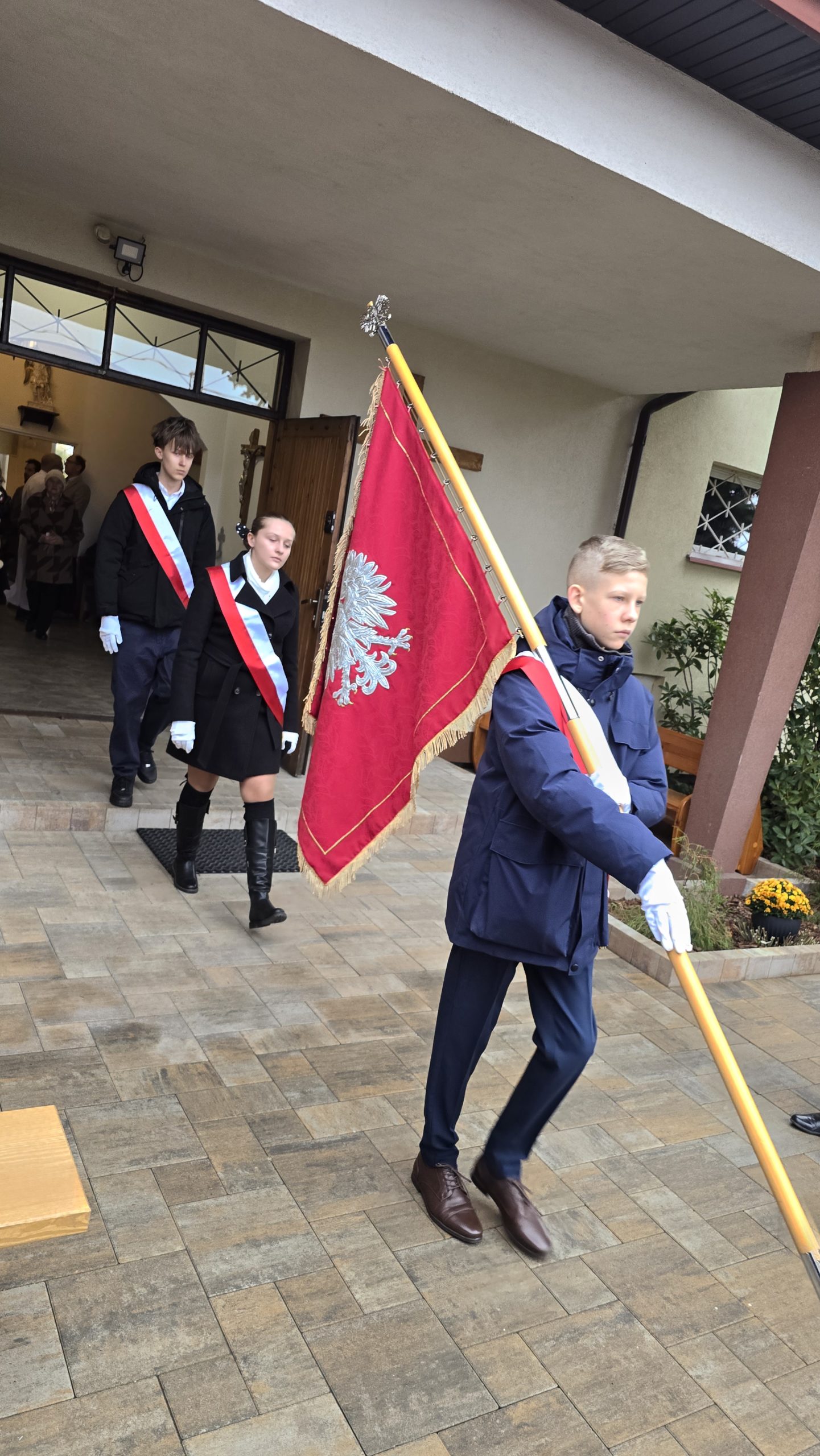 Na obrazku widać postać z flagą oraz idące za nią dwie postacie z założonymi na siebie szarfami w barwach narodowych